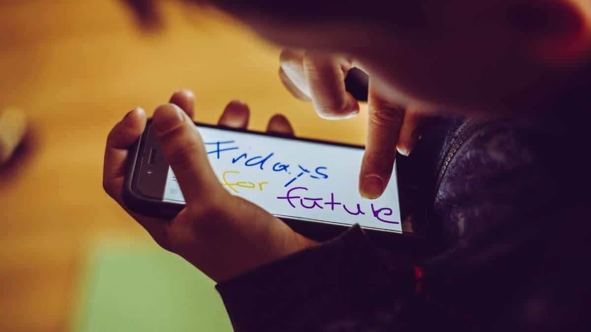 A close-up of a child using a smartphone, highlighting a 'Fridays for Future' message, symbolizing youthful involvement in climate activism.