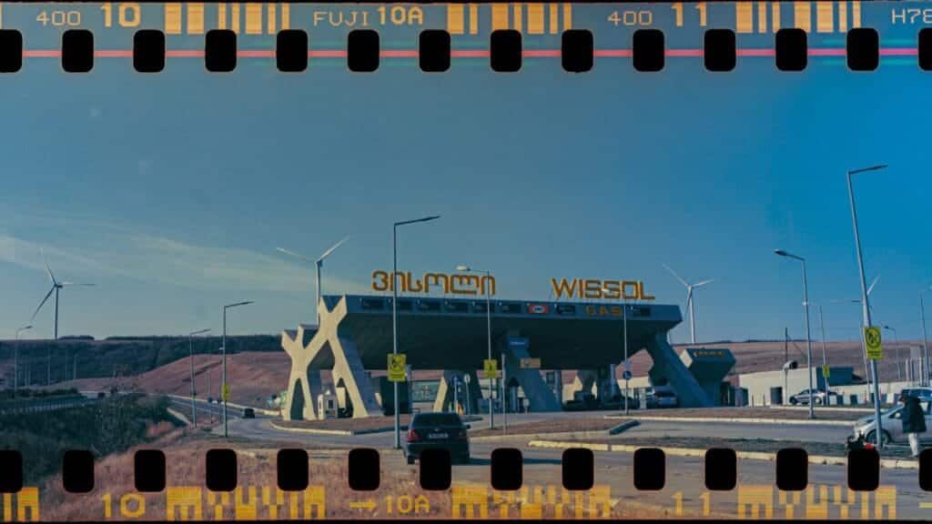 Vintage-style gas station in Gori, Georgia with wind turbines and cars under clear skies.