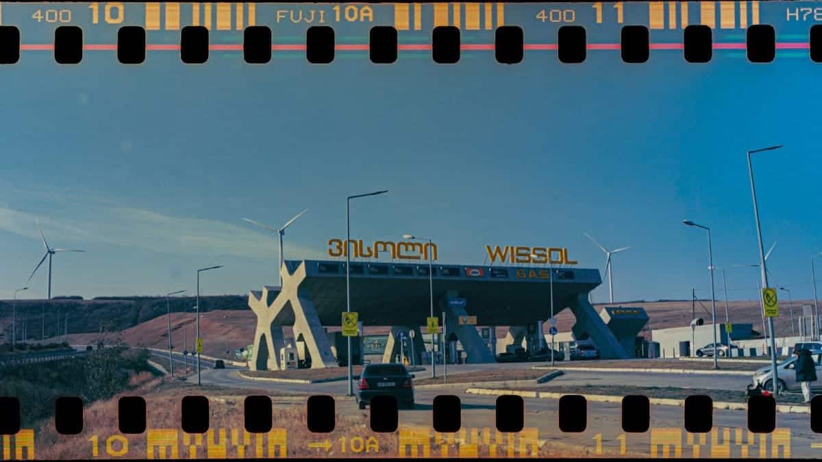 Vintage-style gas station in Gori, Georgia with wind turbines and cars under clear skies.