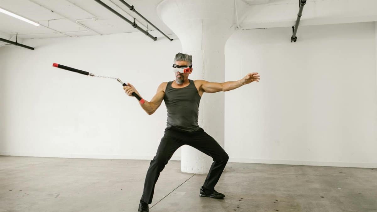 Adult man skillfully using nunchaku with VR headset in an indoor setting, showcasing future tech integration.