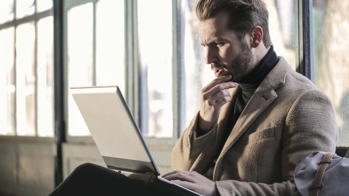 Man looking contemplative while working on a laptop in a well-lit indoor space.