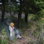 Person camping and enjoying a warm morning coffee in a serene forest setting.