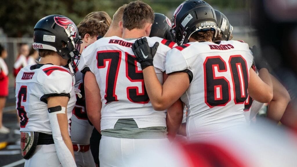 High school football team huddles on the field during a game in Idaho Falls, boosting team spirit.