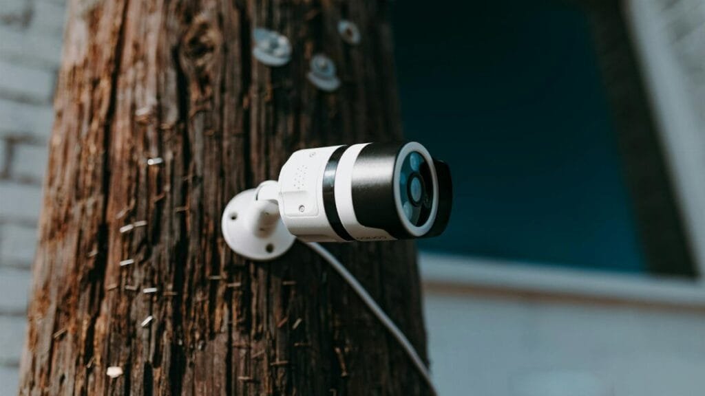Close-up of a modern security camera mounted on a wooden post outdoors.