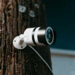 Close-up of a modern security camera mounted on a wooden post outdoors.