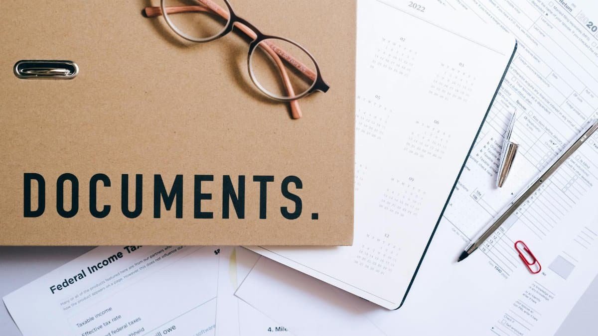 Flat lay of office supplies including documents, calendar, and eyeglasses on a desk.