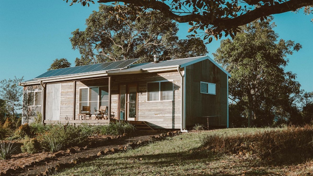 A charming wooden house in Australia featuring solar panels, surrounded by lush greenery.