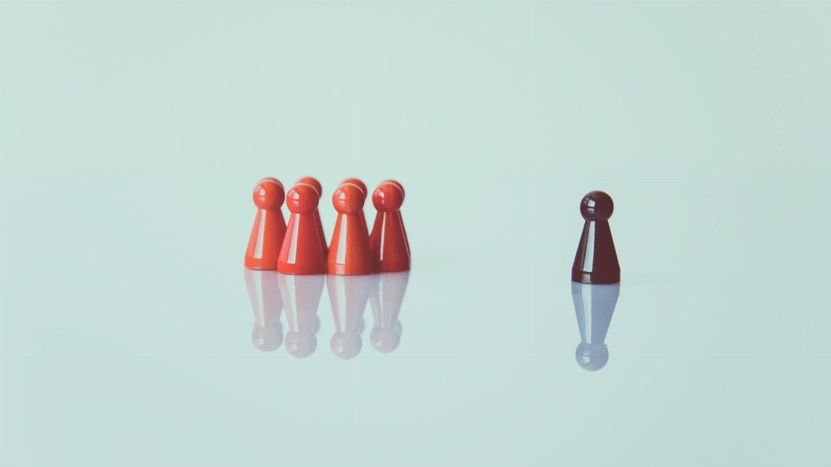 Red game pieces grouped with one isolated piece symbolizing social distancing on a reflective surface.