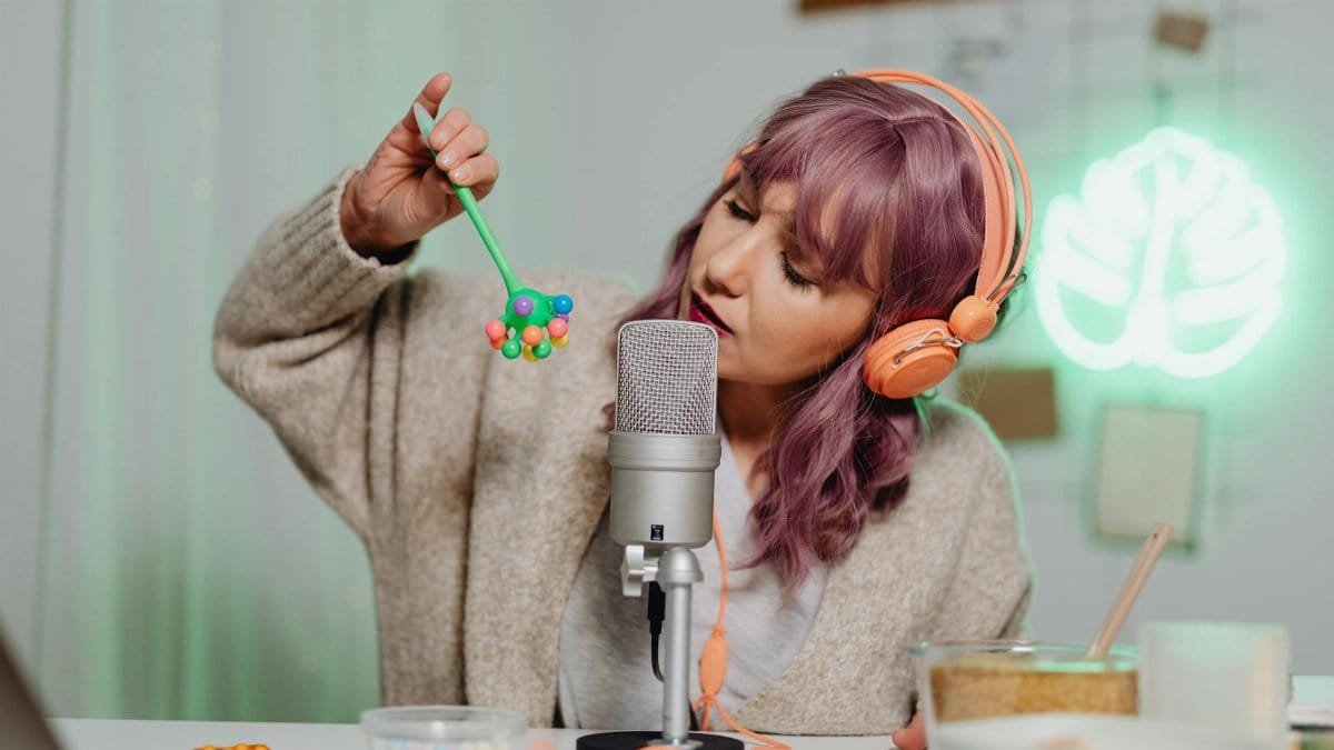 A woman with colored hair engaged in ASMR, using microphone and toy.