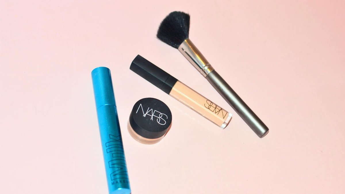 Top view of professional mascara concealer and cosmetic foundation placed near brush for applying makeup on pink background in studio