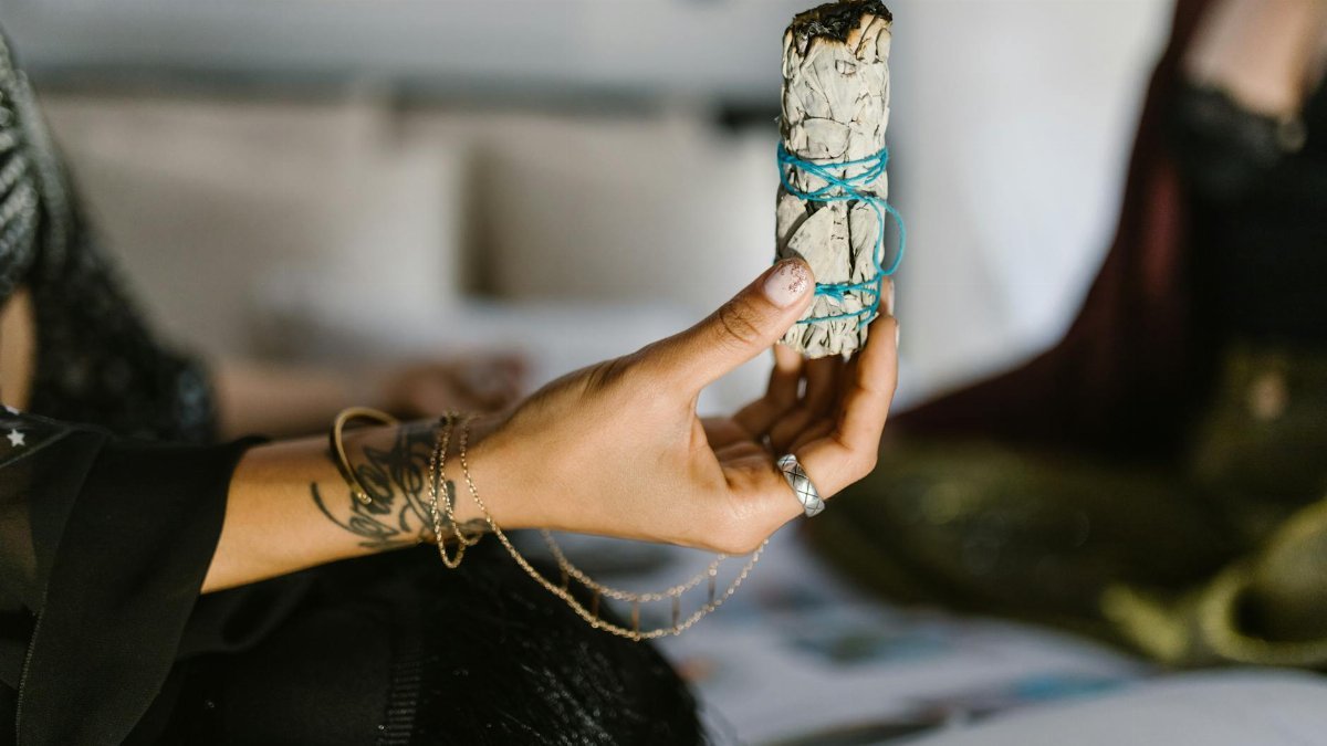 A person holding a sage bundle tied with blue string, often used in spiritual cleansing rituals.