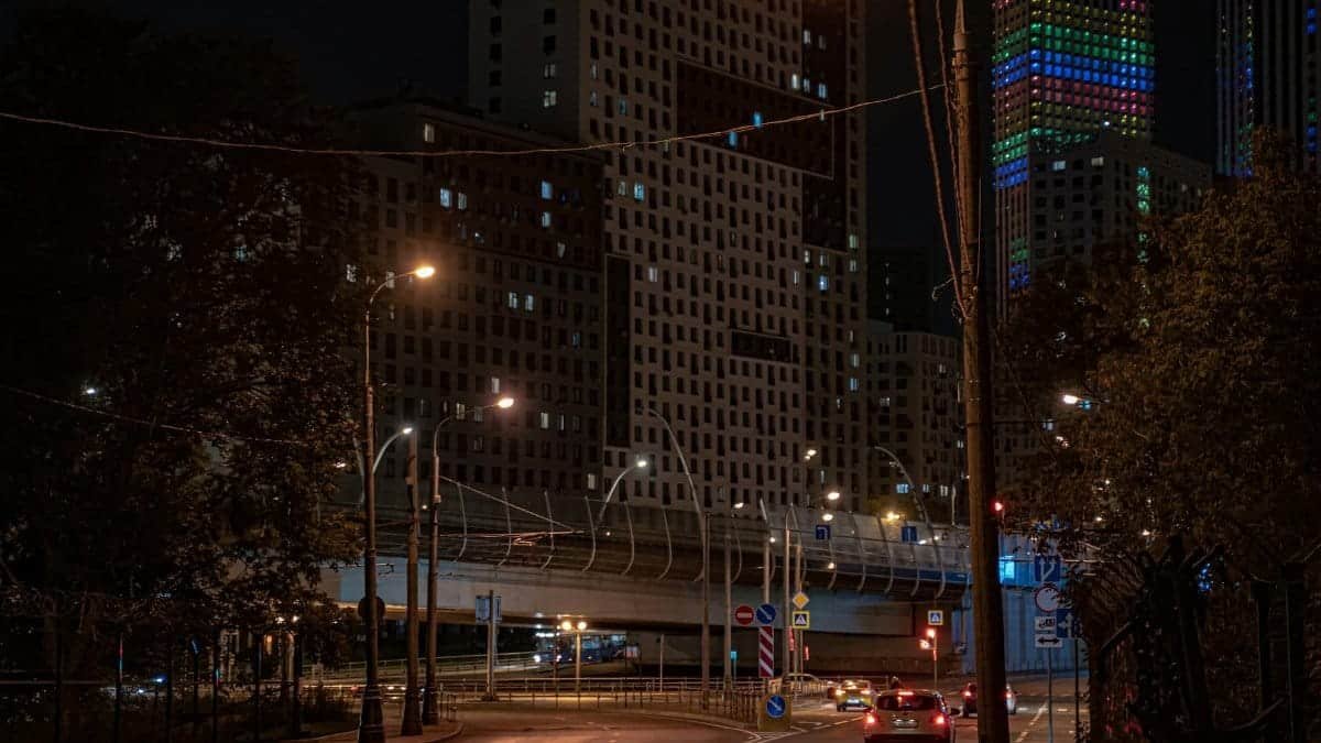 Street view of illuminated buildings and a quiet road at night in a city.