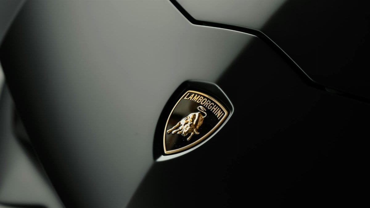 Detailed close-up photo of a Lamborghini logo on a sleek black car hood, symbolizing luxury and style.