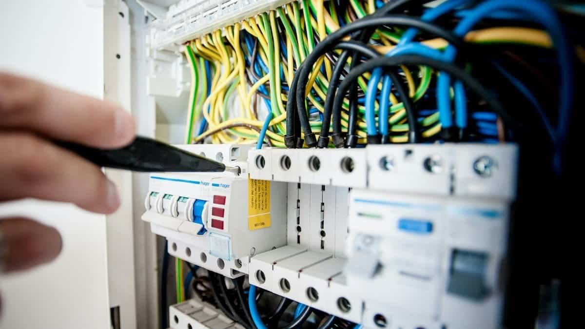 Hand of electrician working on a circuit breaker panel with colorful wires, ensuring safe electrical connections.