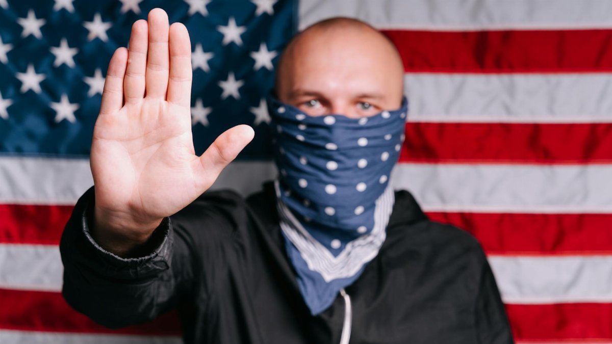 A masked protester gestures in front of an American flag, symbolizing activism.
