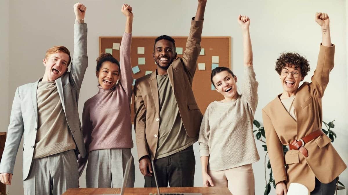 A diverse team celebrating success with raised hands in a modern office setting.