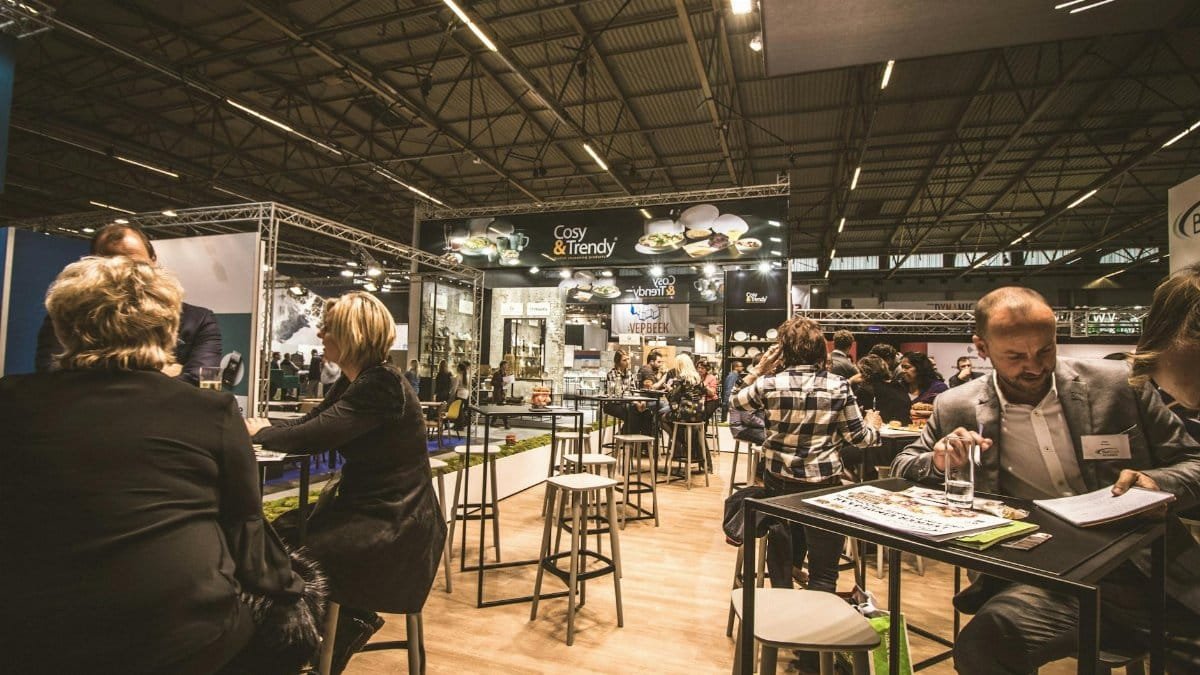 A bustling indoor business expo with professionals networking and engaging at various booths.