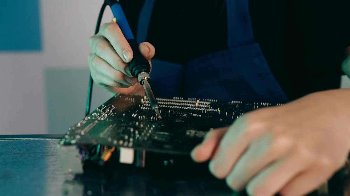 Close-up view of hands soldering electronic components on a circuit board.
