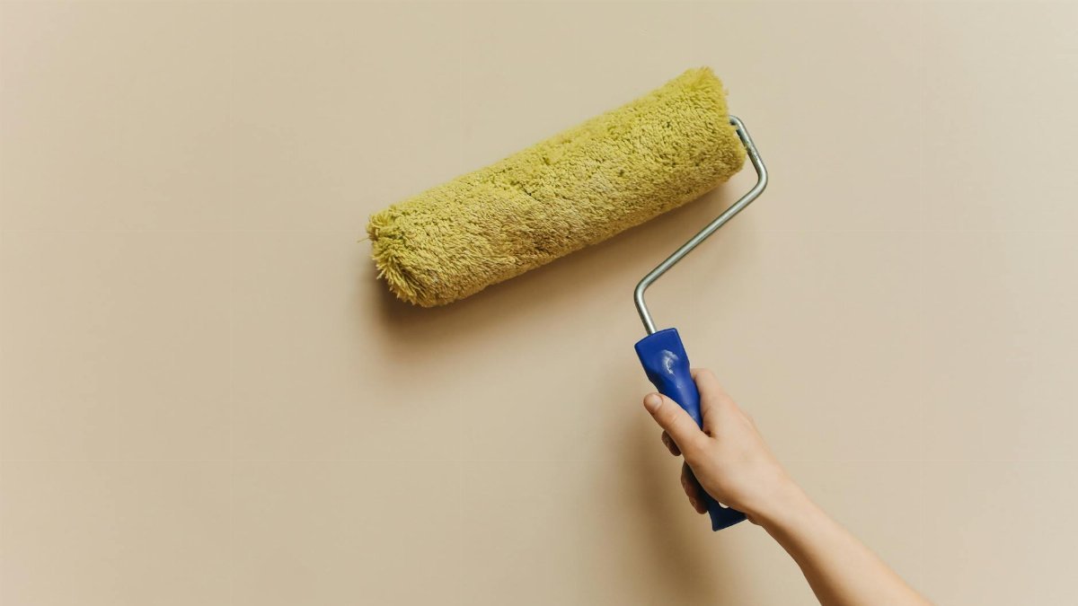 A hand using a yellow paint roller to paint a beige wall. Perfect for DIY and home improvement themes.
