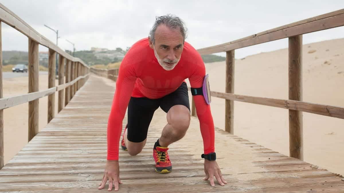 Active senior man in red preparing for a run on a scenic wooden pathway at the beach.
