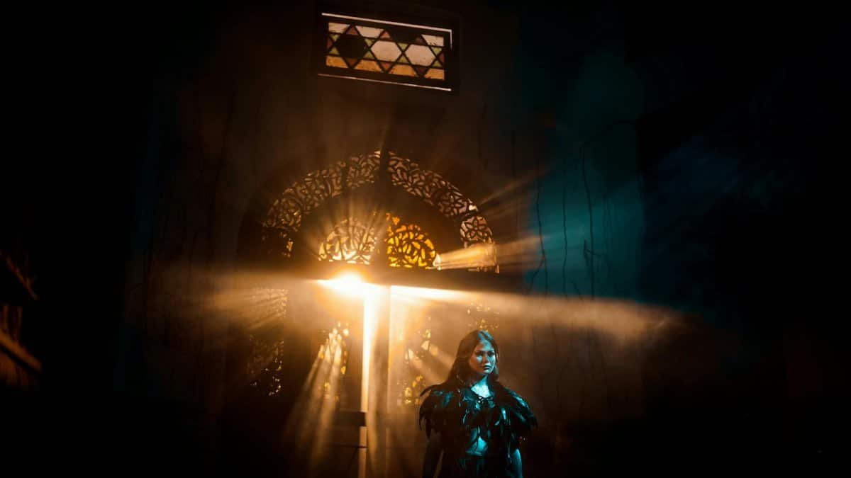 A woman in dramatic lighting poses in an atmospheric setting with rays of light.