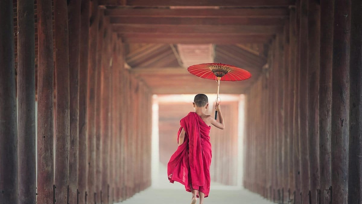 A child monk holding a parasol walks through a traditional Asian temple corridor, embracing cultural heritage.