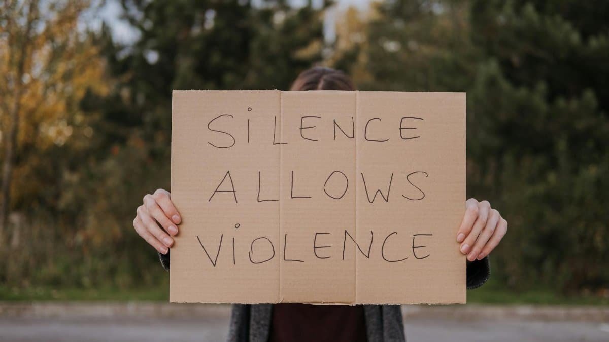 Anonymous person showing slogan silence allows violence on cardboard on road near green trees