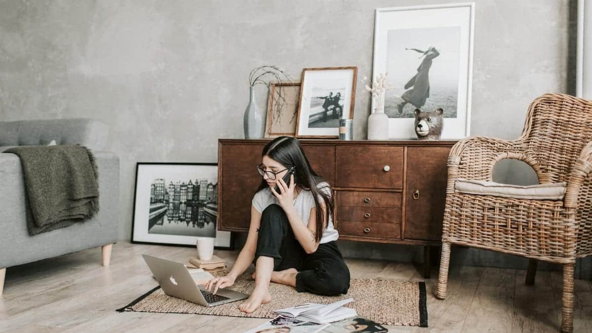 Woman using a laptop and phone in a modern, stylish living room with artistic decor.