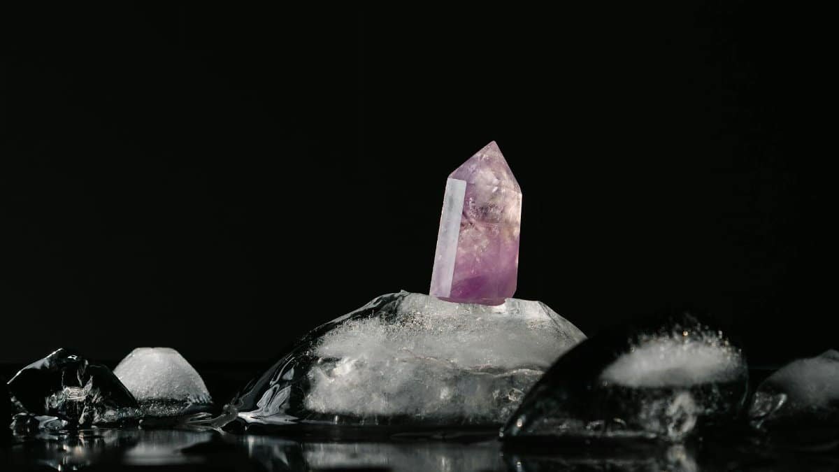 A vivid purple amethyst crystal surrounded by melting ice on a reflective black surface.
