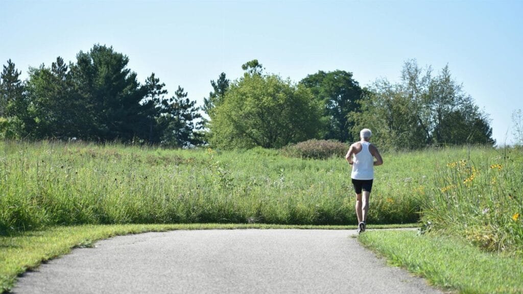 An elderly man jogging on a scenic pathway in a lush green park.