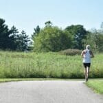 An elderly man jogging on a scenic pathway in a lush green park.