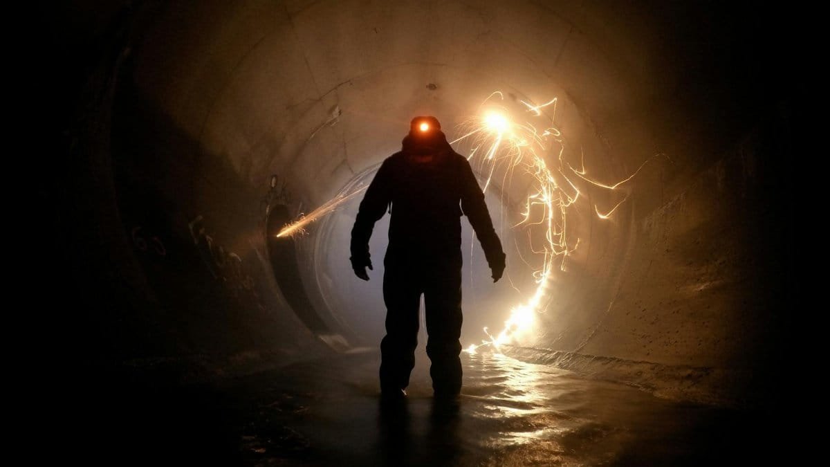 A silhouette of a worker in protective gear inside a tunnel with dramatic light sparks.
