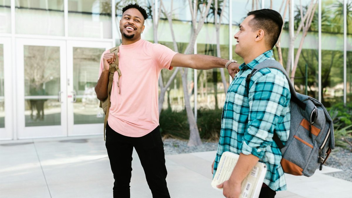 Two college students enjoying a friendly conversation on campus, carrying backpacks.