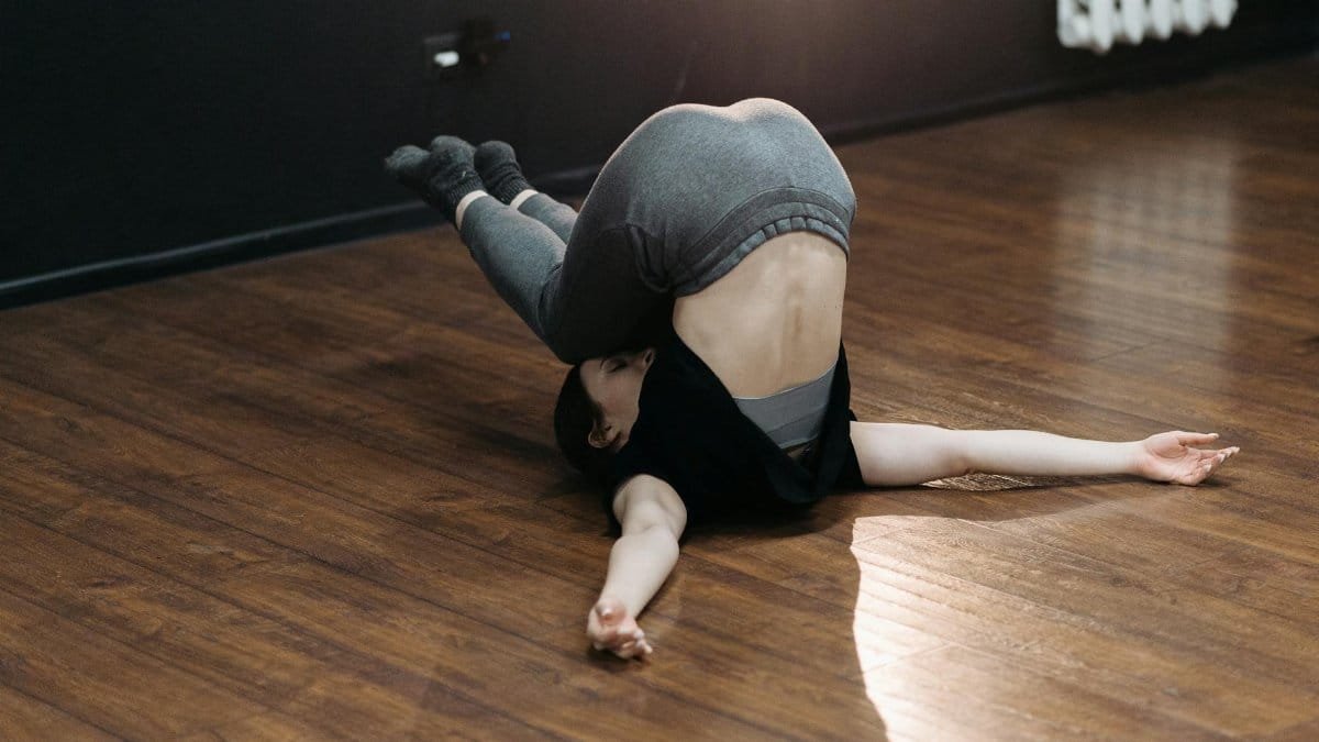 Woman practicing a challenging yoga pose on a wooden floor indoors, showcasing flexibility and balance.