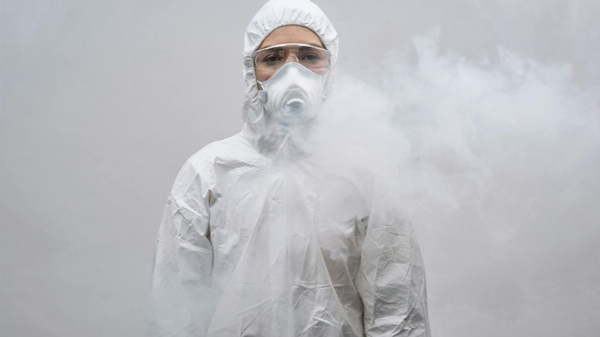 Individual in protective suit and mask standing in smoke on white background.
