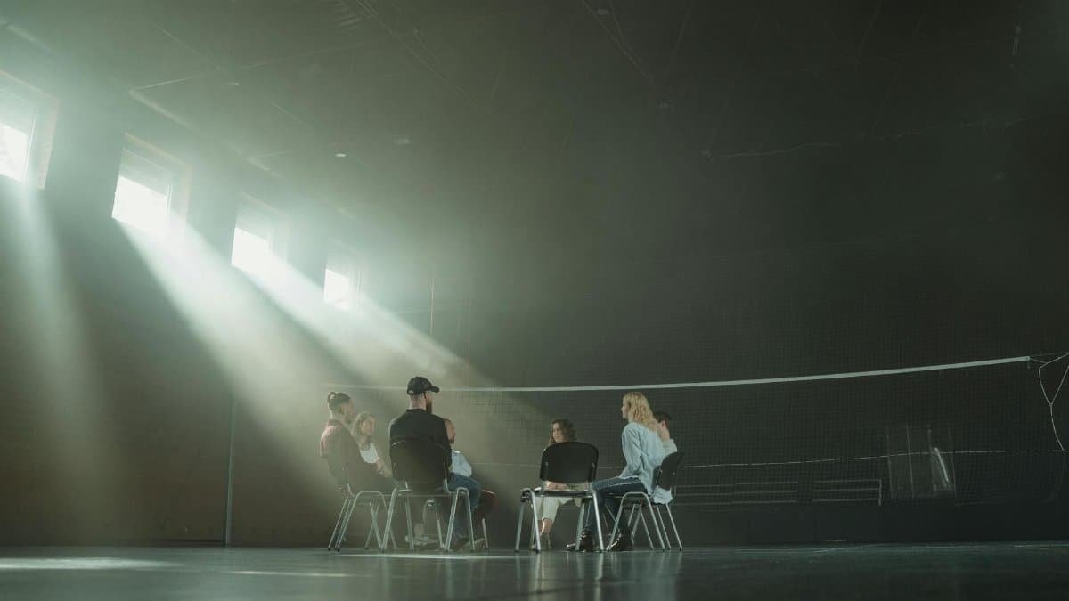 A small group of people participating in a support session, illuminated by sunrays in a spacious hall.