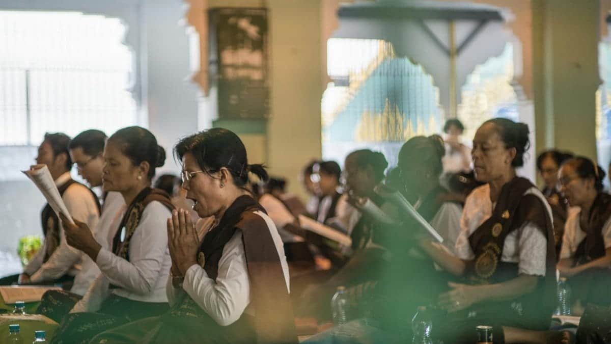 Adults engaged in prayer and meditation inside a Buddhist temple, fostering faith and tranquility.