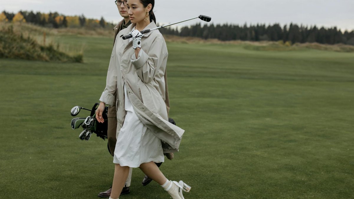 A fashionable couple walking with golf equipment on a lush green course.