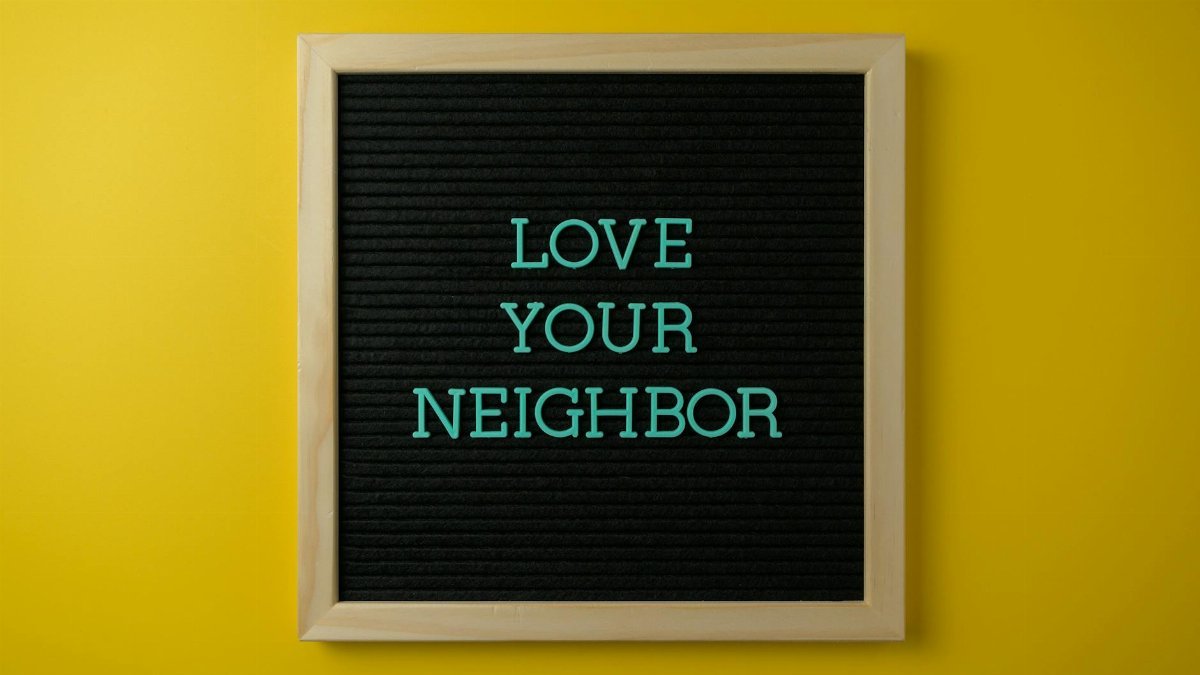 A motivational message "Love Your Neighbor" on blackboard against a yellow wall.