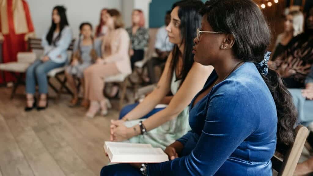 A diverse group of people in a church setting, engaged in prayer and reflection, holding a holy book.