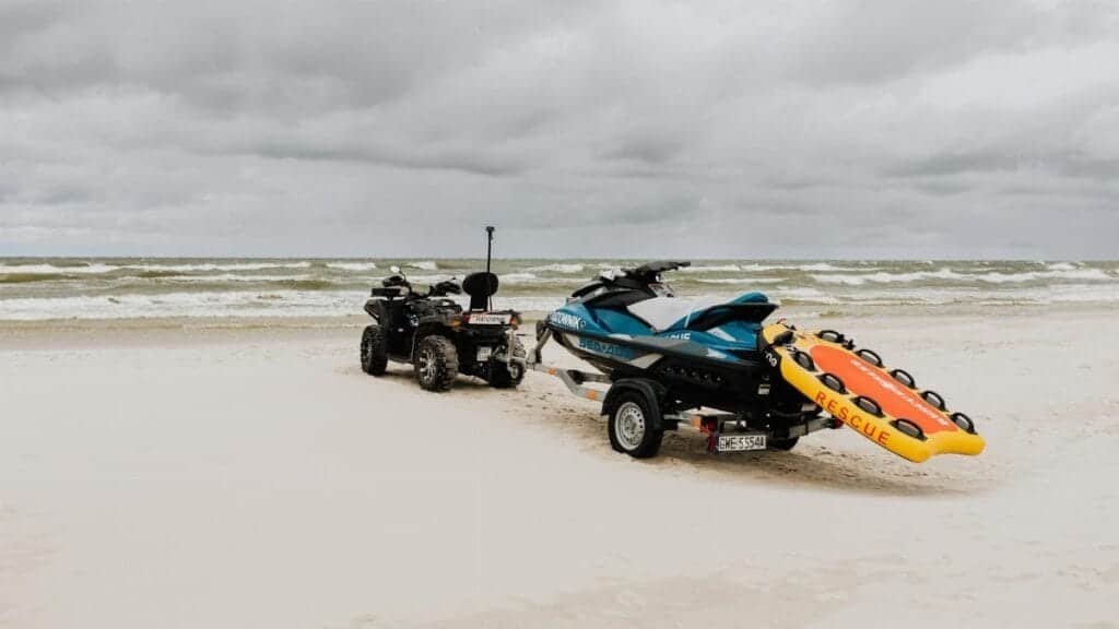 Jet ski and quad bike with rescue equipment on a cloudy beach shore.
