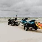 Jet ski and quad bike with rescue equipment on a cloudy beach shore.