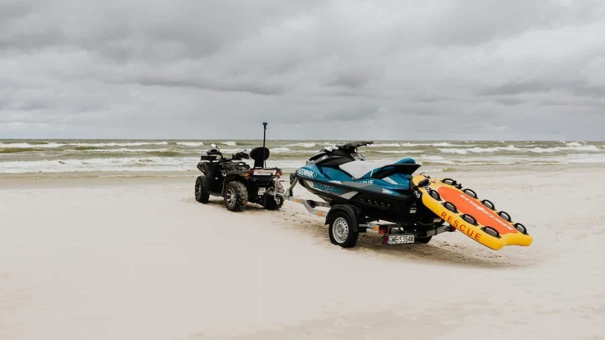 Jet ski and quad bike with rescue equipment on a cloudy beach shore.