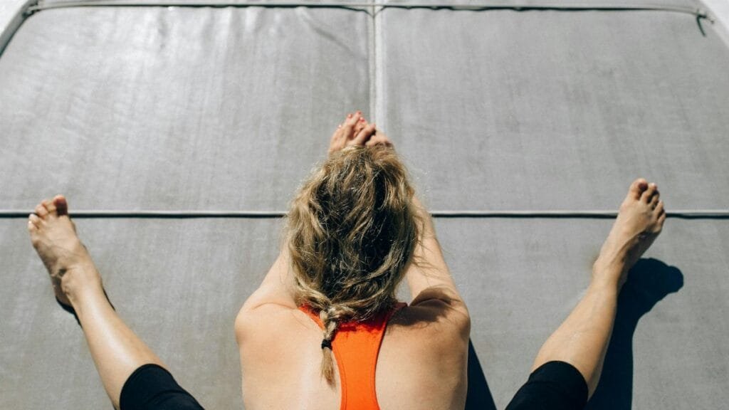 Woman practicing yoga on a mat outdoors, stretching on a sunny day.