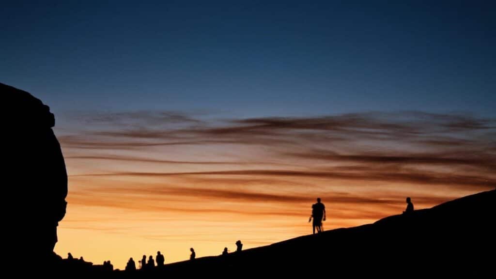 A striking scene of silhouetted people against a vibrant sunset sky on a rocky landscape.