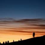 A striking scene of silhouetted people against a vibrant sunset sky on a rocky landscape.