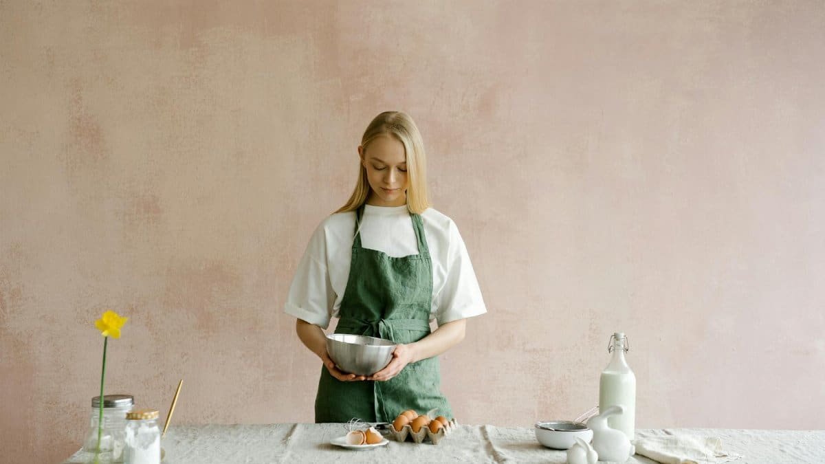 A woman in an apron prepares ingredients on a rustic kitchen table, ready to bake.