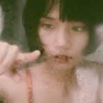 Through window of young Asian woman drawing on wet glass with finger in soft light