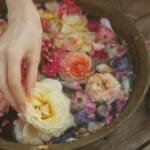 A hand gently arranges colorful flower petals floating in a rustic wooden bowl.