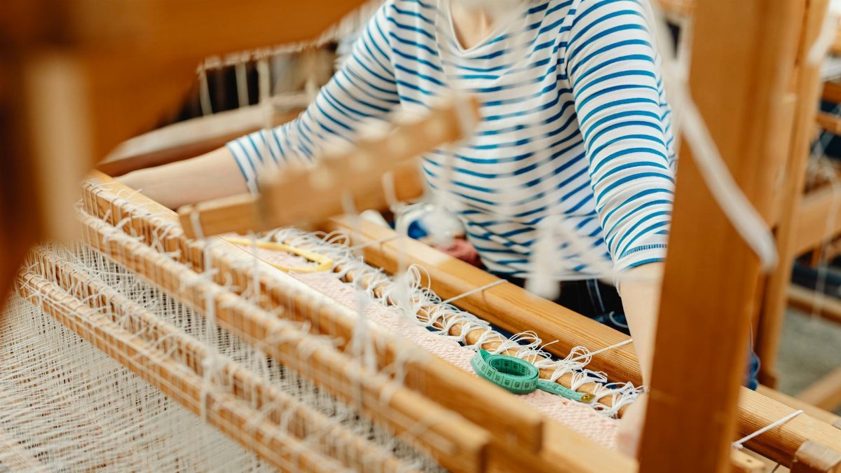 A close-up view of a person weaving on a wooden loom with threads intricately arranged.
